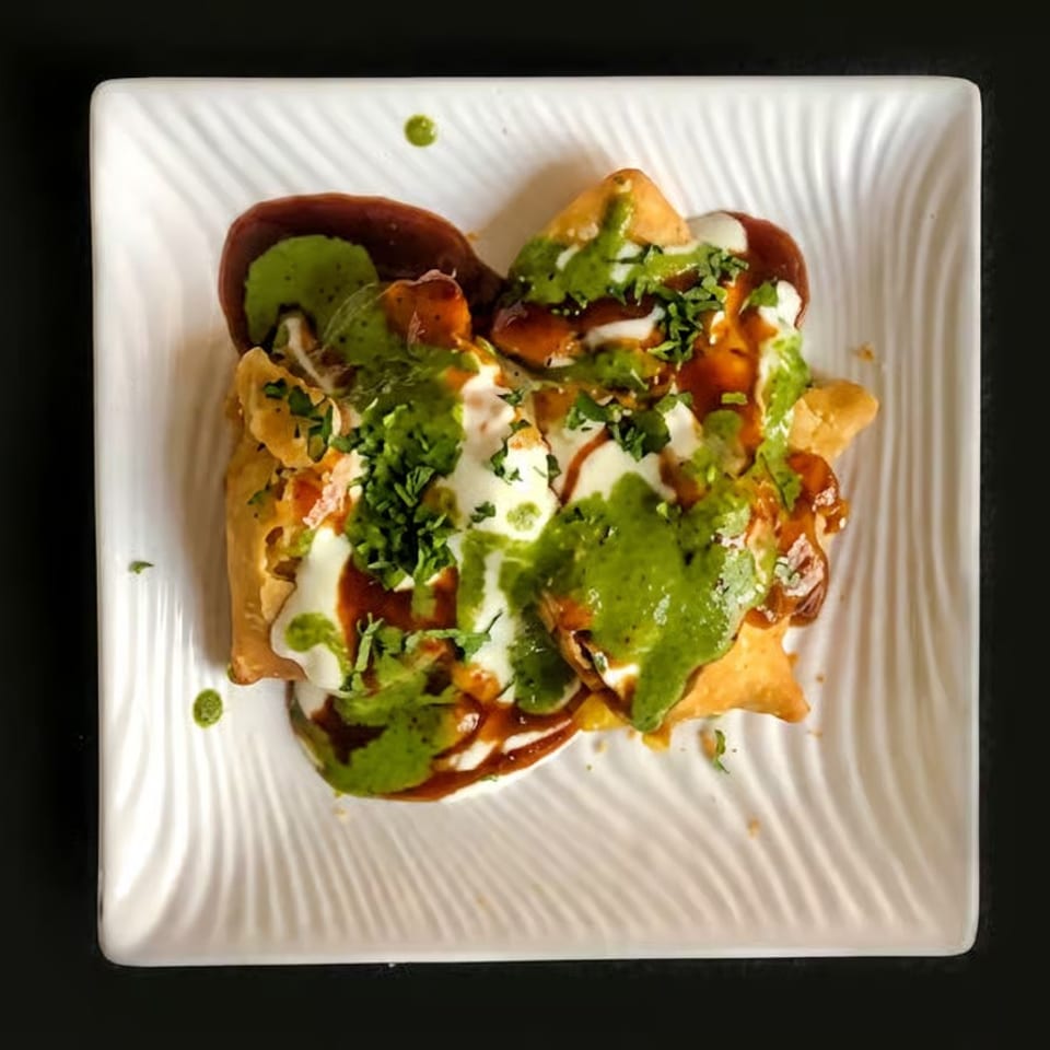 Crispy nachos topped with green salsa, white crema, red sauce, avocado, and chopped cilantro on a square white plate.