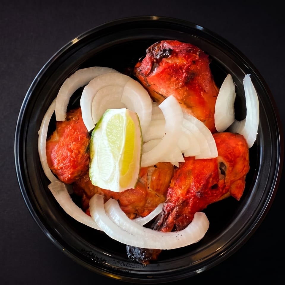 Grilled chicken pieces topped with sliced onions and a lime wedge in a black bowl.